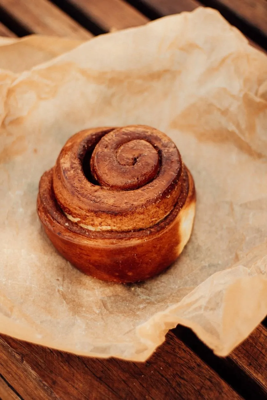 A single glazed cinnamon bun sitting on crumpled baking paper