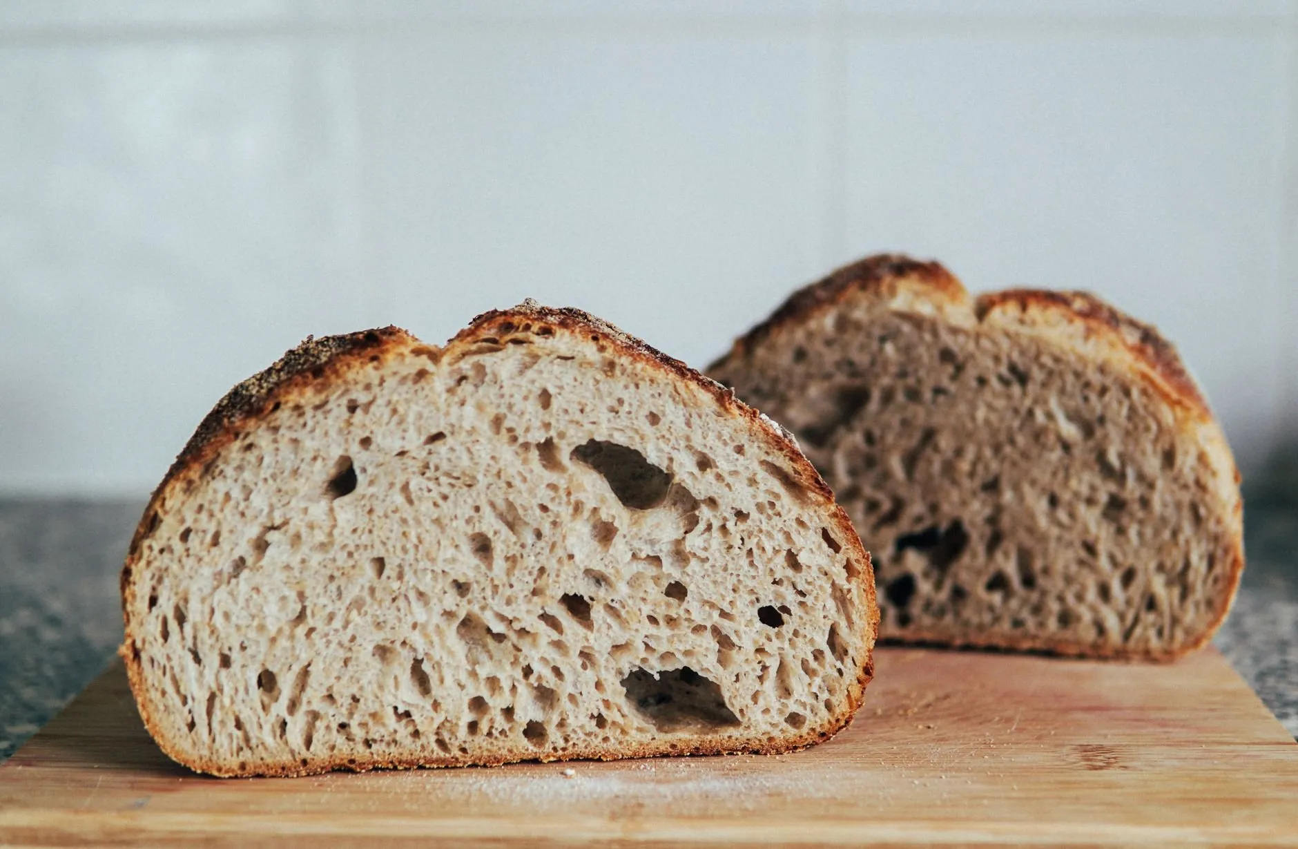 Two halves of a large round spelt loaf on a wooden board, showing a soft open crumb