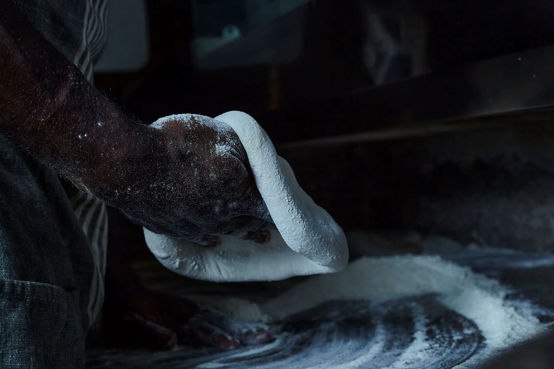 A baker's floured hand working dough on a dark bench